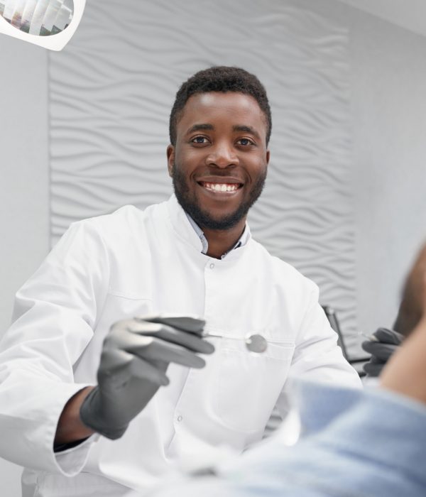 Selective focus of cheerful male dentist in process of curing teeth in dentist office. Professional doctor looking at camera and laughing while patient lying on dentist chair. Concept of stomatology.