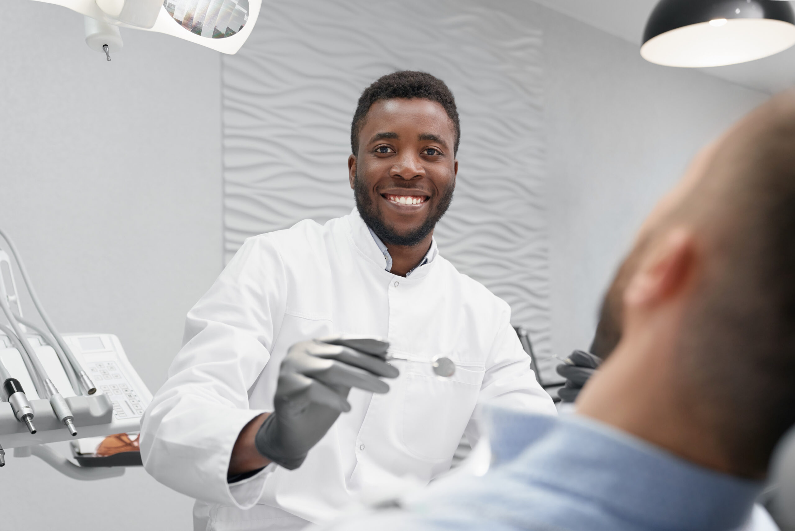 Selective focus of male dentist in process of curing teeth Selective focus of cheerful male dentist in process of curing teeth in dentist office. Professional doctor looking at camera and laughing while patient lying on dentist chair. Concept of stomatology.